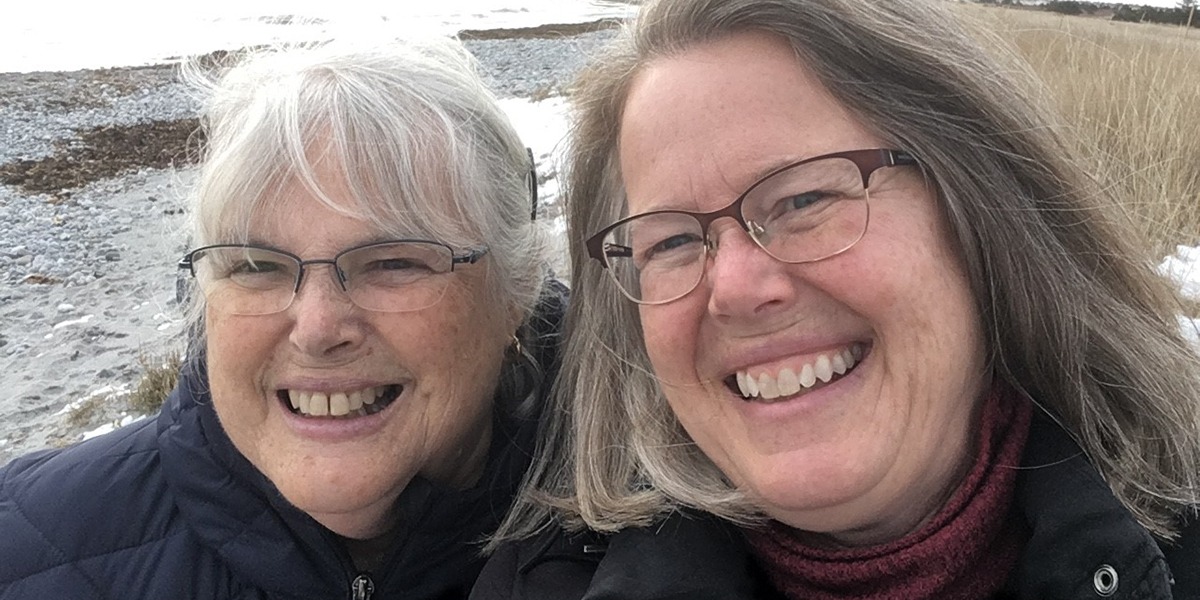 Two women, Aileen and Julie, smiling as they take a selfie on the beach