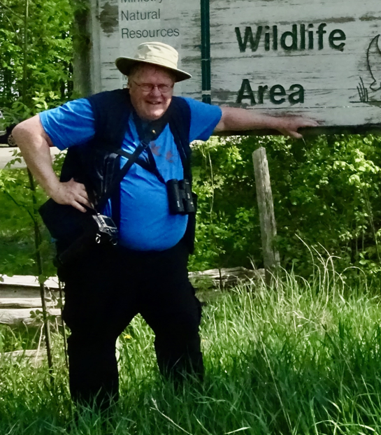 Arthur Needles poses in front of a provincial wildlife area in full birding gear.